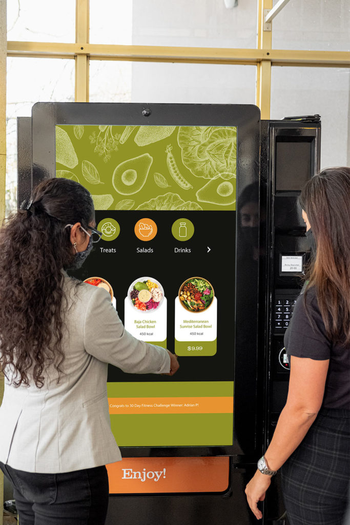 Two people navigating the SmartVending Machine's touch screen, browsing through the various healthy food options. 